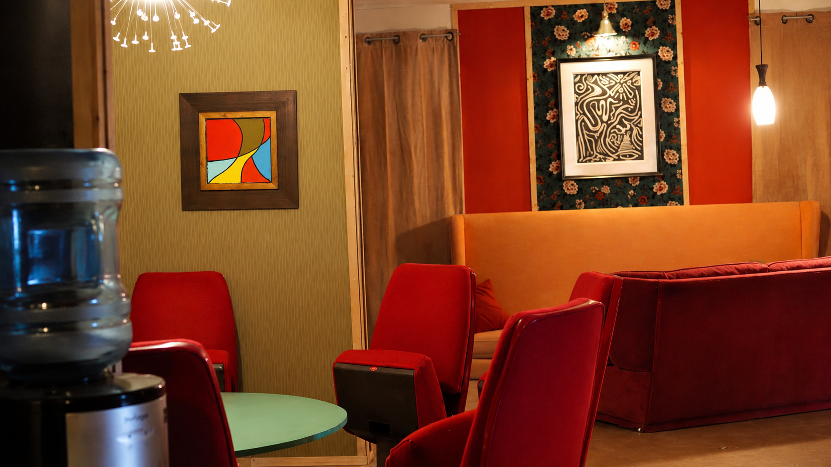 Seating area with red upholstered chairs, a mint table, and colorful wall art